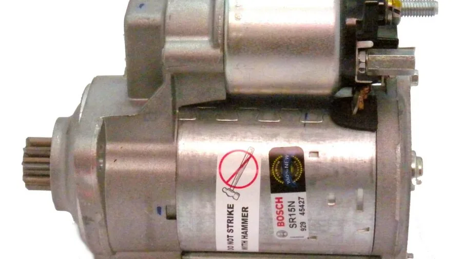 Person working on small motor components at a workbench with tools and parts scattered around