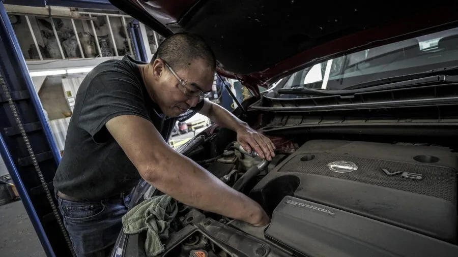 Person working on vehicle exterior in natural daylight, hands-on automotive maintenance scene