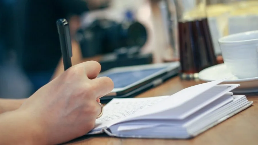 Person writing in notebook at desk, representing practical security habits and digital organization