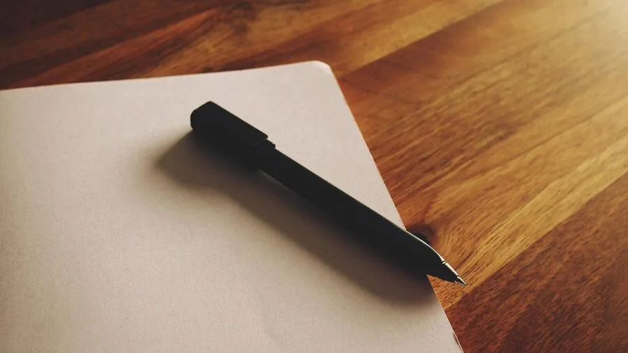 Person writing on documents at a clean desk with office supplies and natural lighting