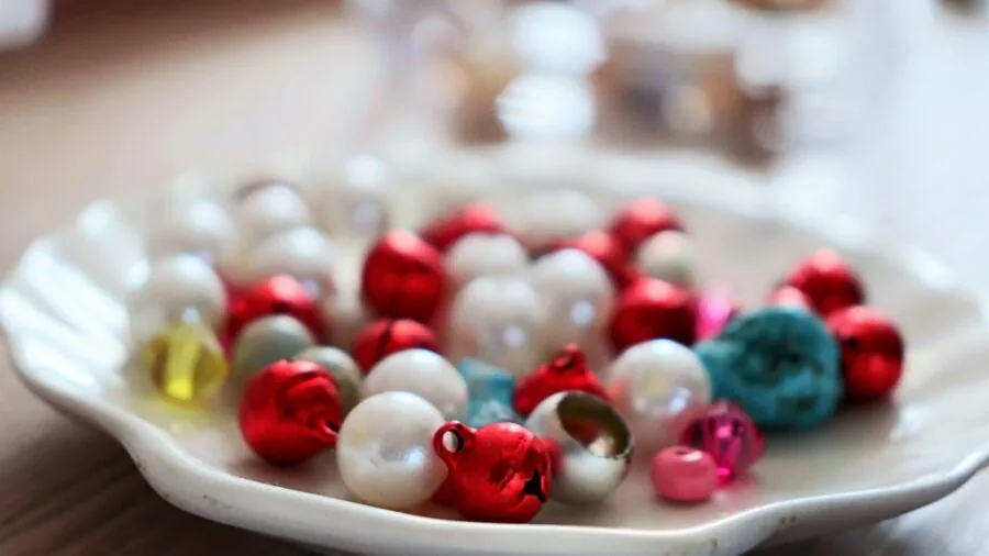 Person's hands arranging colorful beads on wooden surface during beading craft project