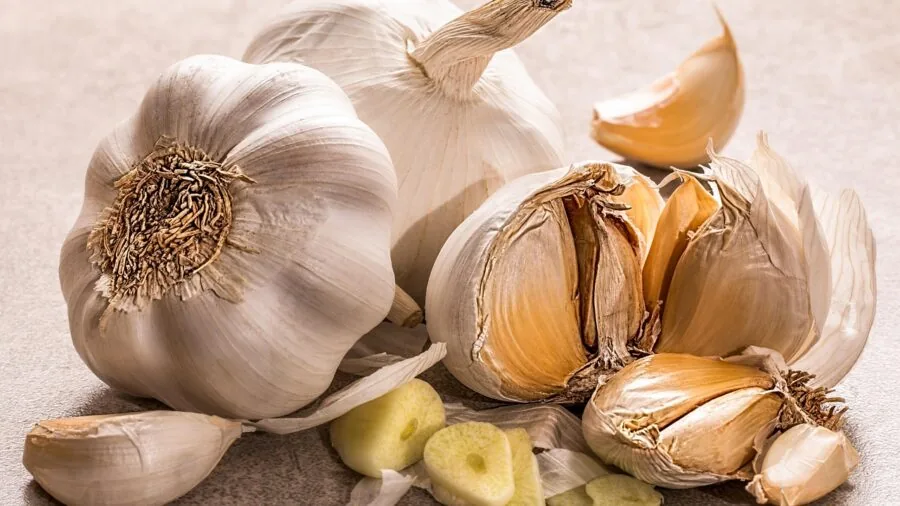 Person's hands breaking apart fresh garlic cloves on a wooden cutting board in a bright kitchen