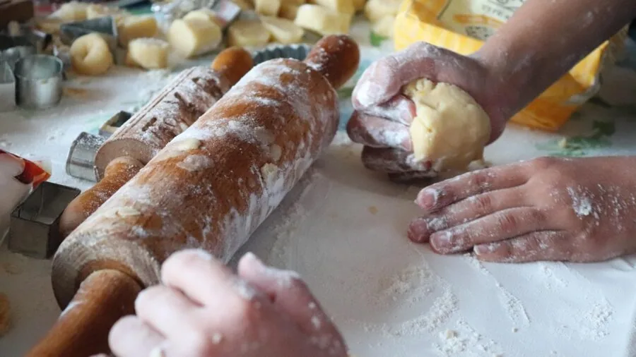 Person's hands cutting cookie shapes from dough on a wooden baking surface