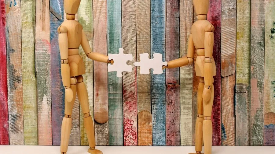 Person's hands fitting together colorful puzzle pieces on wooden table during leisure activity