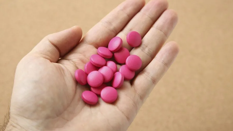 Person's hands precisely cutting a pill in half with a pill cutter device on a wooden surface