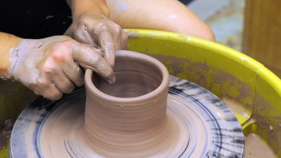 Potter's hands centering small clay on pottery wheel during ceramic creation process