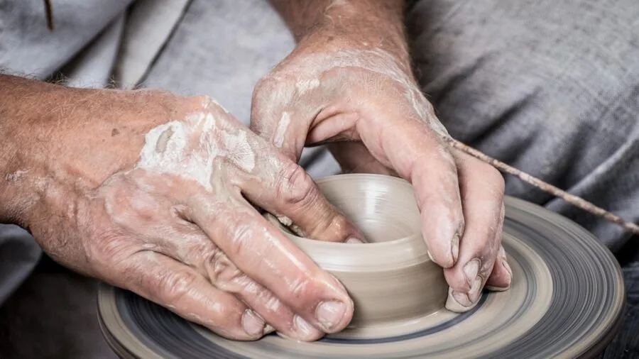 Potter's hands working with clay tools and water bowl at pottery wheel during ceramic creation process