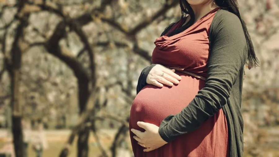 Pregnant woman examining and comparing different sized maternity clothing items in a bedroom setting