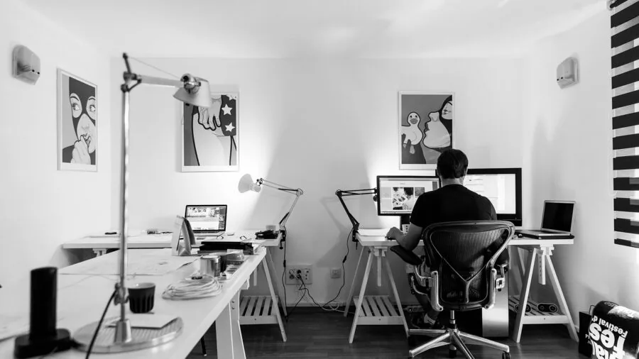 Professional adjusting monitor arm at desk workspace with multiple screens and natural lighting
