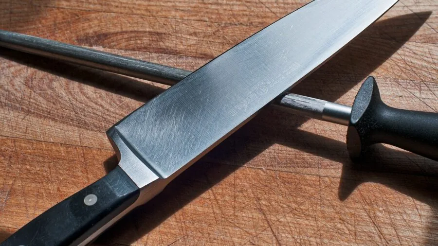 Professional chef carefully sharpening a kitchen knife on a whetstone in natural light
