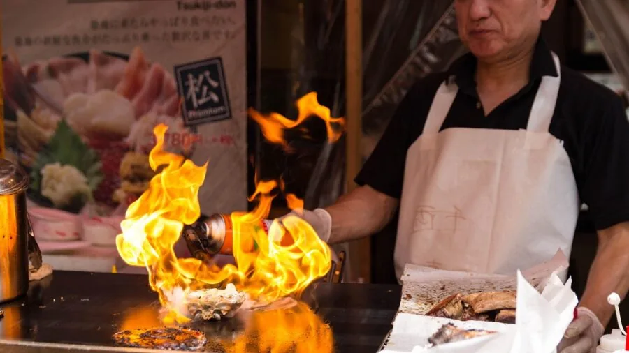 Professional chef cooking with tongs at stovetop, maintaining safe distance from heat and flames