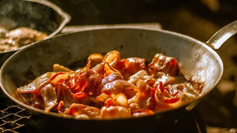 Professional chef searing meat in heavy-duty skillet on stovetop, demonstrating heat retention and cooking technique