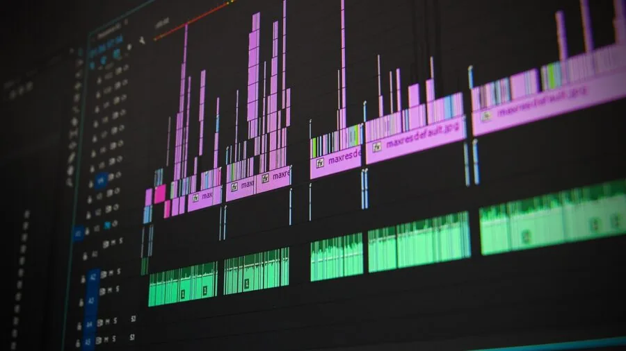 Professional editor working at desk with multiple monitors displaying video timeline and project files