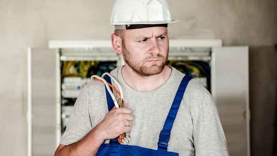 Professional electrician performing electrical safety testing and inspection in residential panel room