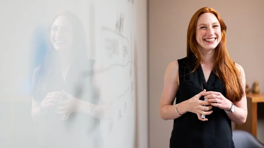 Professional in casual office setting writing notes on whiteboard during work session