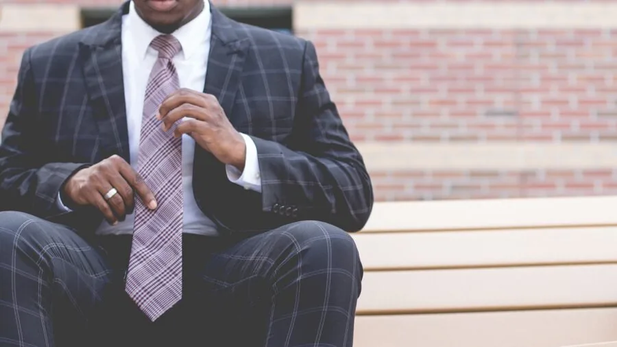Professional man adjusting necktie while wearing suit jacket in natural lighting