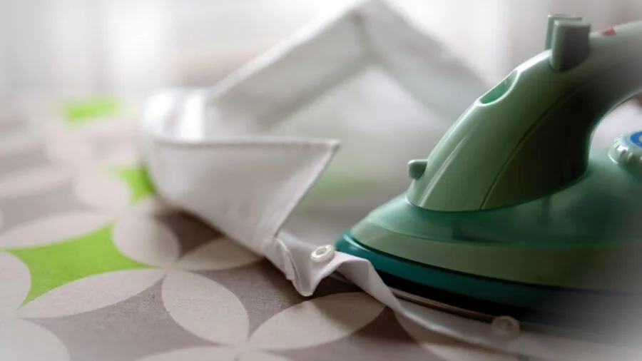 Professional man ironing a dress shirt at home, demonstrating garment care and wrinkle maintenance