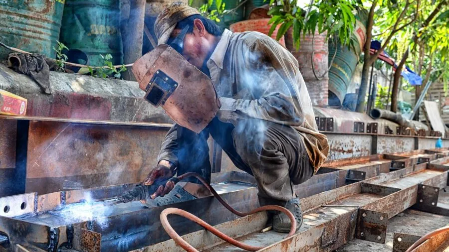Professional welder in protective gear working with metal in industrial workshop setting