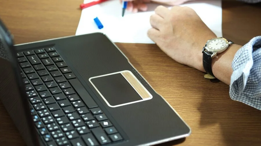 Professional working on laptop at desk with notebook and coffee, representing productive workspace setup