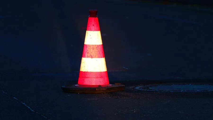 Reflective safety cone visible at night on dark road with vehicle headlights approaching