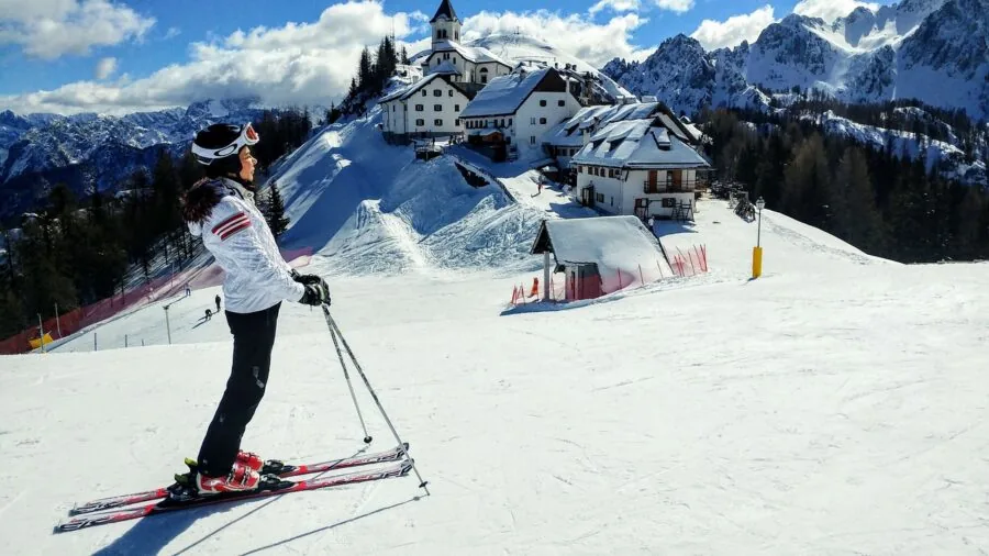 Skier checking and adjusting pole length on snowy mountain slope before skiing