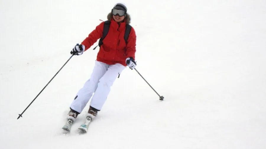 Skier checking boot bindings on snowy mountain slope before descent