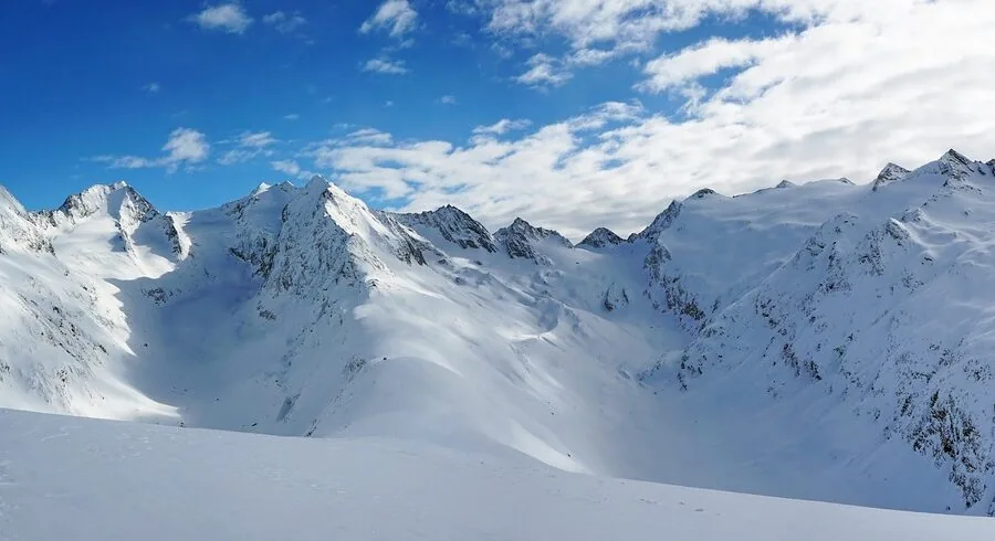 Skier descending a well-groomed ski run on a snowy mountain slope during daytime