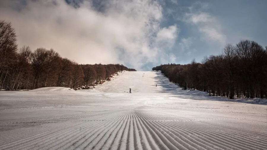 Skier in winter gear adjusting ski boot bindings on snowy mountain slope before descending