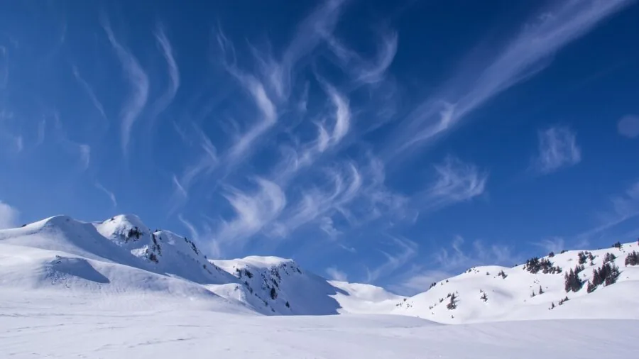 Skier in winter gear on snow-covered mountain slope with visible breath in cold air