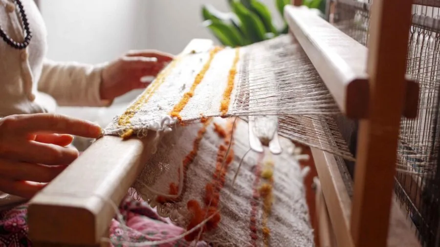 Skilled craftsperson examining different weaving loom options in a textile studio workshop