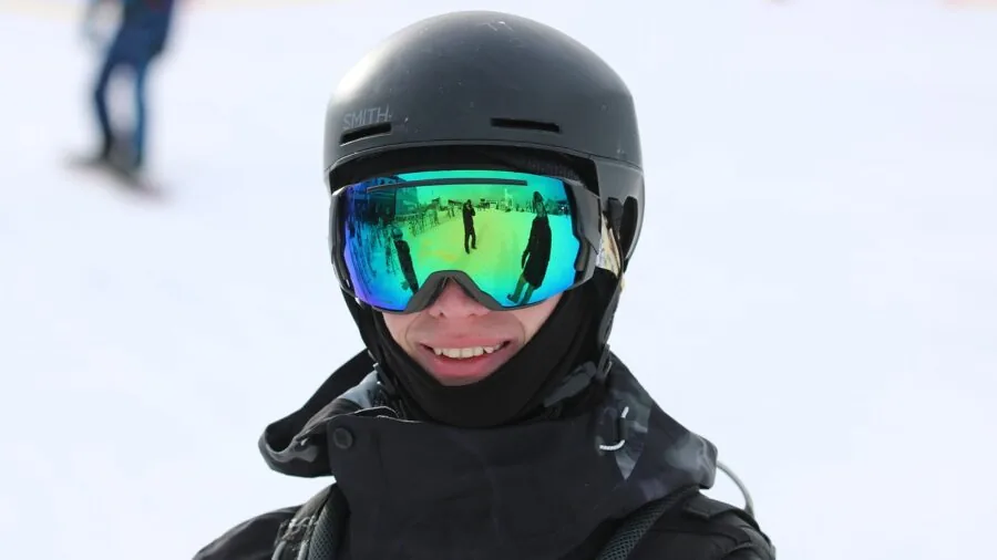 Snowboarder in winter gear adjusting bindings and boots on snowy slope