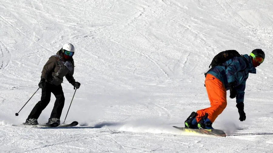 Snowboarder sitting in snow adjusting boot lacing system before riding down snowy mountain slope