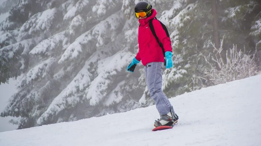 Snowboarder tightening and adjusting boot straps before riding down snowy mountain slope