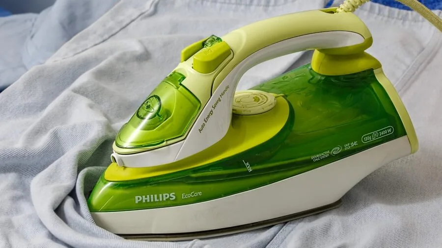 Someone carefully steaming lightweight cotton clothing at home with a handheld steamer