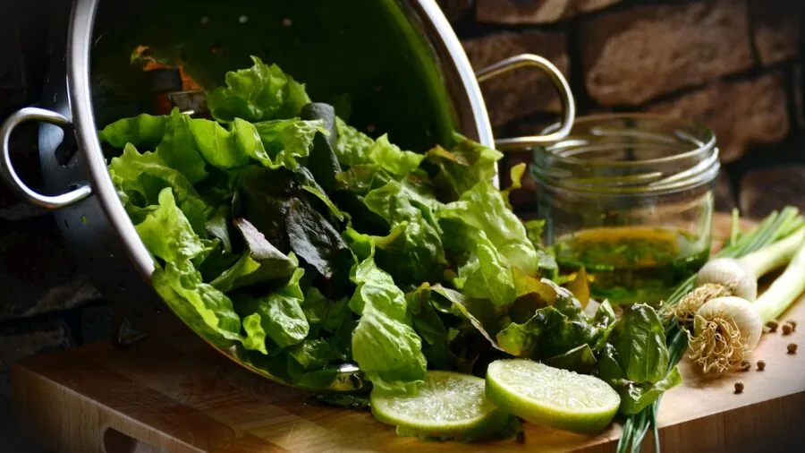 Someone's hands washing and preparing fresh greens in a kitchen sink for salad preparation