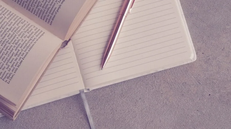 Student writing in open notebook at desk with study materials and coffee cup