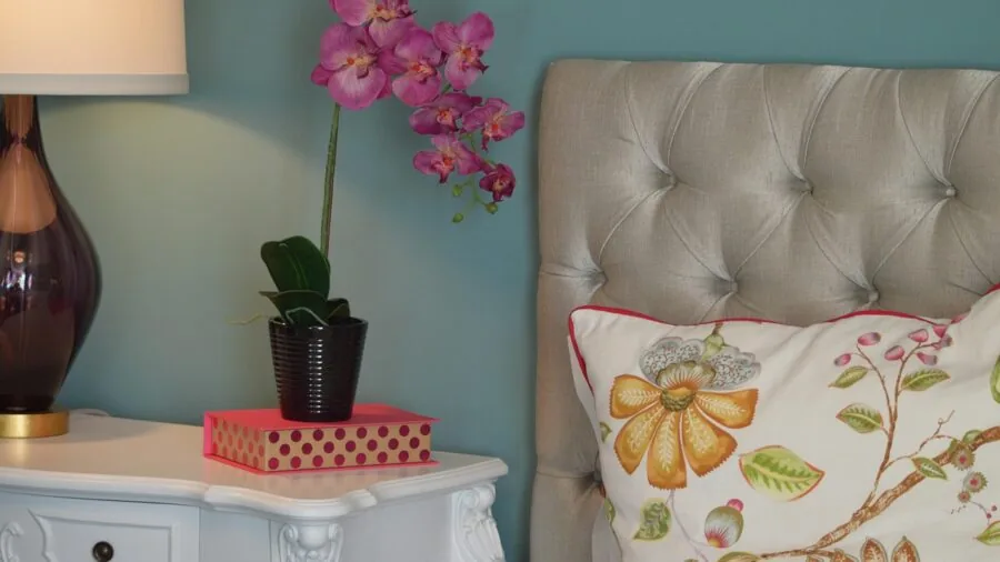 Styled bedroom nightstand with lamp, plants, and decorative items next to bed