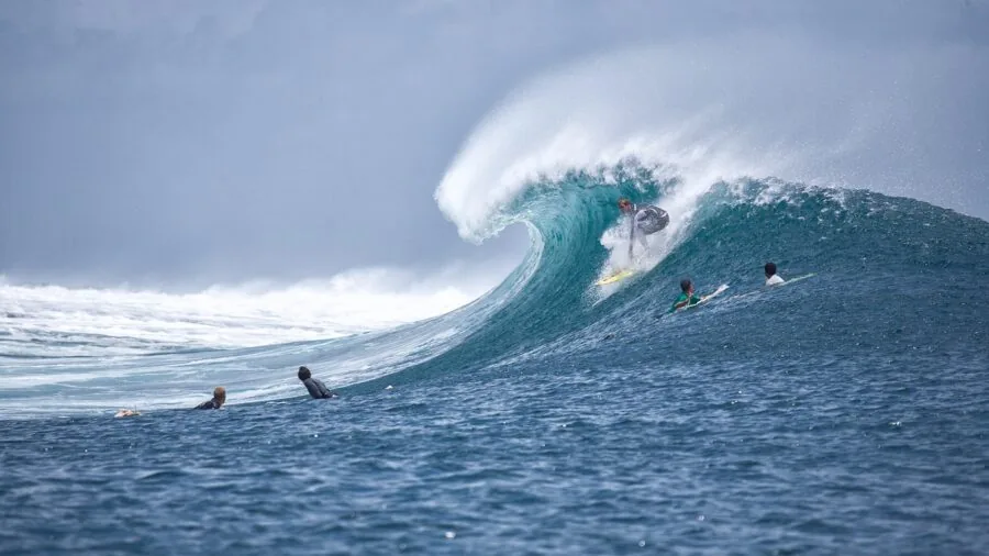 Surfer arranging surfboard with leash and fins on sandy beach before paddling out