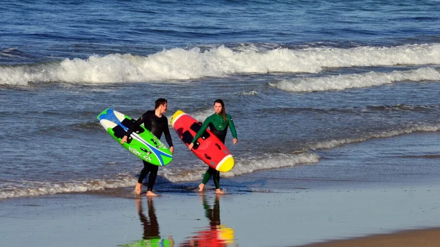 Surfer examining different surfboards lined up on sandy beach before choosing one