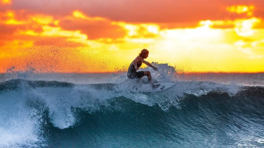 Surfer inspecting and adjusting fins on surfboard in shallow water before paddling out