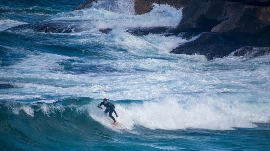 Surfer riding a bodyboard on a blue ocean wave during golden hour
