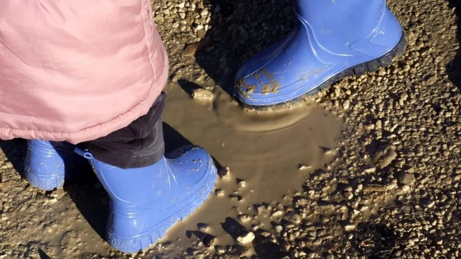 Toddler in oversized rain boots playing in puddles outdoors