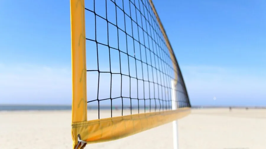 Two people assembling a portable volleyball net on a beach or outdoor court
