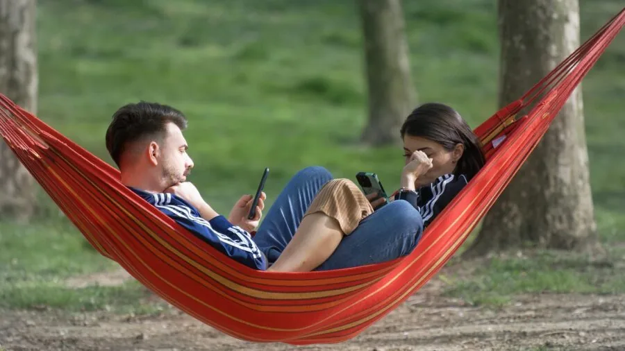 Two people enjoying a hammock together in a residential backyard setting on a sunny day