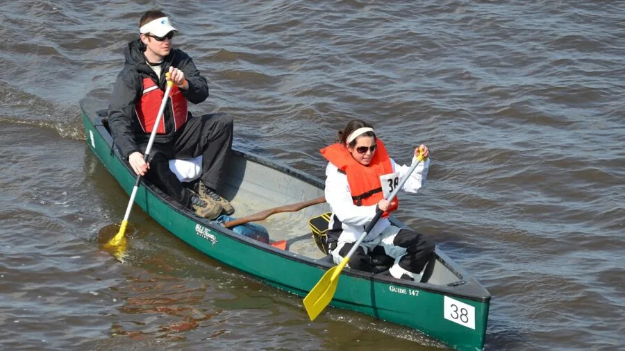 Two people paddling a tandem kayak on calm water during daytime outdoor recreation