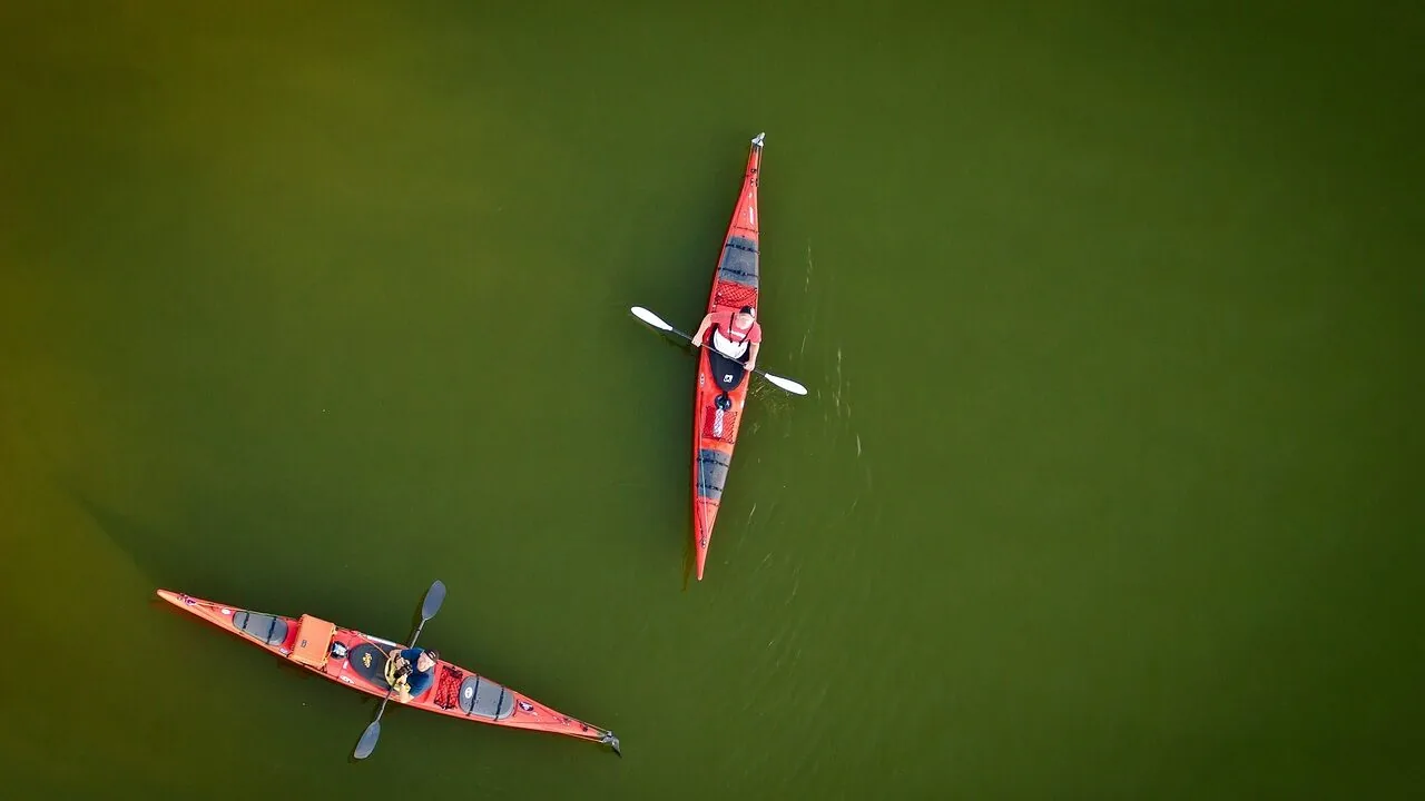 Two-person tandem kayak on calm lake water with paddles