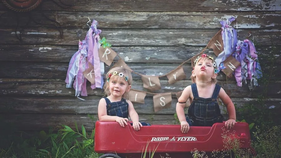 Two young children sitting together in a wagon outdoors during family activity