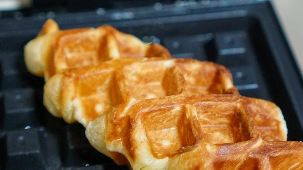 Waffle maker cooking fresh waffles on kitchen counter