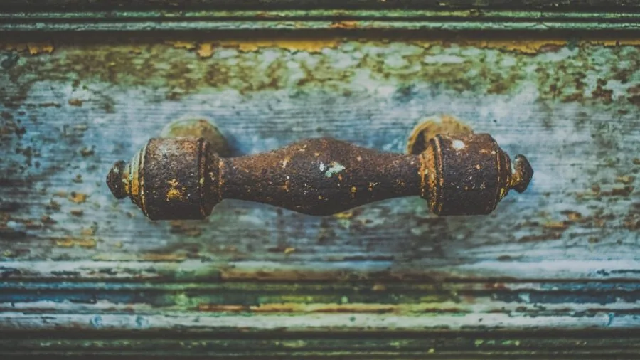 Weathered wooden door showing rust and corrosion damage from exposure to elements and coastal salt air