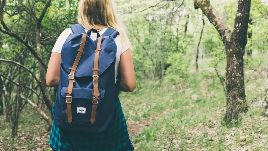 Woman adjusting backpack shoulder straps while hiking on a forest trail